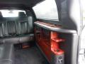 Interior of a 2008 Cadillac Limousine featuring black leather seats and an elegant red wood panel with storage and cup holders