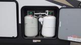 A compartment containing two propane tanks secured and connected with valves and gauges visible