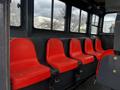 Five red seats with seatbelts arranged in a row inside a vehicle with large windows along the sides