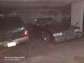 A 1982 Mercury Grand Marquis parked in a garage next to an SUV featuring a long hood and classic design with chrome detailing and a dark exterior color