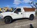 A white 2000 Ford F-350 SD with a metal bed and black wheels parked on a surface with visible dirt and wear