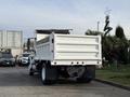 A 2015 International DuraStar 4300 white dump truck with a flatbed and rear tailgate parked in a lot