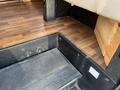 Close-up of the step and flooring inside a 2012 Ford Econoline showing textured rubber surface and wood flooring beneath a beige seat