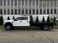 A white 2021 Ford F-550 flatbed truck is parked on the street side profile view with a black flatbed and a dual rear wheel setup