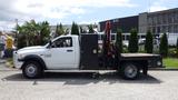 A 2014 RAM 5500 flatbed truck with a black utility box and a red hydraulic crane attached to the bed