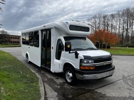 A white 2017 Chevrolet Express bus with a front entrance and large windshield parked on a paved surface