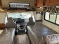 Interior view of a 2012 Ford Econoline with two front seats and a living area featuring a leather couch and wooden cabinets