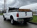 A white 2011 Ford F-250 SD pickup truck with a metal bed cover and loaded with wooden crates in the truck bed