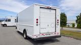 A 2011 Ford Econoline delivery van with a white exterior and a rear roll-up door parked on a paved surface