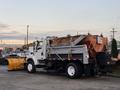 A 2006 Freightliner M2 106 truck equipped with a snow plow and a large orange salt spreader in the truck bed