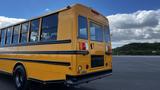 A yellow 2014 Freightliner Thomas Diesel school bus seen from the rear with large windows and a black stripe along the side