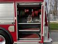 A red 1994 Freightliner FL80 with an open storage compartment showing coiled hoses and tools inside two shelves