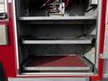 Interior storage compartment of a 1994 Freightliner FL80 with two metal shelves and hydraulic equipment visible on the top shelf