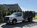 A white 2016 Ford F-350 SD flatbed truck with a black metal frame and no cover parked on a street