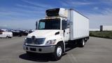 A white 2009 Hino 268 box truck with a refrigerated unit on top and a flat front design is parked, featuring a prominent brand logo on the grille and clear side mirrors