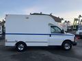 A 2009 GMC Savana van with a white body and a blue stripe on the side featuring a boxy cargo area and chrome wheels