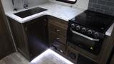 A kitchen area featuring a sink with a marble countertop an oven with knobs and multiple drawers in a 2021 Forest River 312BH East To West Della Terra