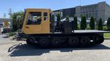 A 2015 PowerBully Tracked Flat Deck Equipment Carrier with a yellow cab and black tracked wheels designed for terrain mobility and heavy equipment transport