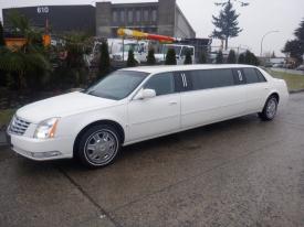 A white 2008 Cadillac limousine with a sleek design and chrome wheels parked on a street