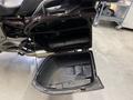 A 2013 BMW K1600GTL motorcycle storage compartment is open revealing a black interior with a user manual and space for items