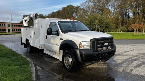 A white 2007 Ford F-550 service truck with a utility bed and a ladder rack on top is parked with its front facing the viewer