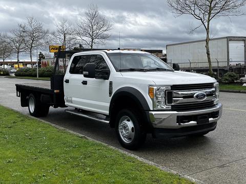 A white 2017 Ford F-550 truck with a flatbed and chrome front grille parked on a street