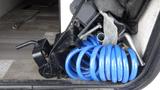 A blue coiled hose is partially visible next to a black hitch and various metal tools inside the storage compartment of a Forest River 312BH East To West Della Terra camper