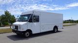 A white 2011 Ford Econoline delivery truck with a large cargo area and front headlights illuminated