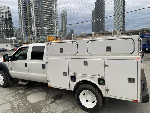 A 2015 Ford F-450 Super Duty truck with a white utility service body featuring multiple storage compartments and a diesel engine