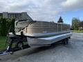 A 2013 Sylvan 13 person pontoon boat with a beige exterior and a covered rear section is attached to a trailer