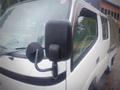 A white 2003 Toyota Toyoace featuring a side mirror with raindrops and part of the cab visible in the foreground