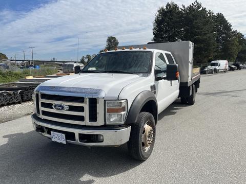 A 2010 Ford F-550 with a white exterior and a flatbed design parked on a street