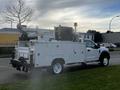 A 2018 Ford F-550 truck with a white utility bed equipped with various storage compartments and mounted equipment on the back