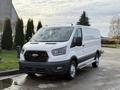 A white 2023 Ford Transit van with a streamlined design and black grille parked in a driveway