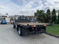 A 2012 Ford F-550 flatbed truck with a metal mesh back and wooden planks on the bed parked on a concrete surface