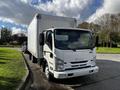 A white 2016 Isuzu NPR truck with a boxy cargo area parked on the side of the road