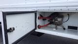 A white truck with the door open revealing a compartment containing a mechanical component and red hoses connected to it