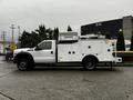 A white 2015 Ford F-550 utility truck with a raised service body and equipment compartments on the sides