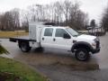 A white 2009 Ford F-450 SD flatbed truck with a utility box in the bed and a yellow light on the roof