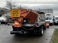 A 2009 Ford F-550 truck with a large orange spreader attached to the back featuring a warning sign that reads STAY BACK 15 m