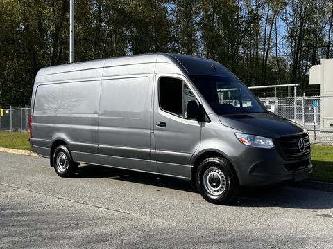 A 2021 Mercedes-Benz Sprinter van in silver with a high roof and long body design parked on a gravel surface