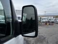 A side mirror of a 2016 Mercedes-Benz Sprinter with a black casing showing a reflection of nearby vehicles