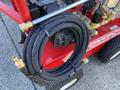 A red 2024 Magnum 4000 Hot Water Pressure Washer with a coiled black hose secured with a plastic tie and various controls and attachments visible on the unit