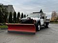 A white 2009 Ford F-550 truck with a silver utility bed and a large orange snow plow attached to the front