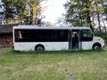 A 2005 Workhorse Glaval LF72 passenger bus with an open door and black-tinted windows parked on grassy terrain