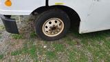 A 2006 Ford Econoline with a visible wheel showing rust on the rim and a partially worn tire resting on grass and gravel