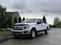 A white 2018 Ford F-150 pickup truck is parked on a paved surface with a sleek design and chrome accents