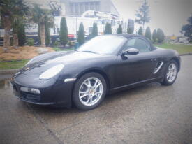 A black 2006 Porsche Boxster with a convertible top and five-spoke alloy wheels parked on a wet surface