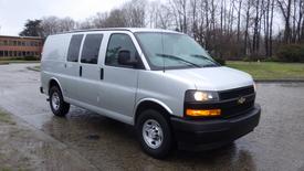 A silver 2018 Chevrolet Express van is parked with its front facing slightly to the right and its side door visible