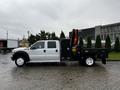 A 2014 Ford F-550 truck with a flatbed and a red crane attachment on the rear side facing to the left